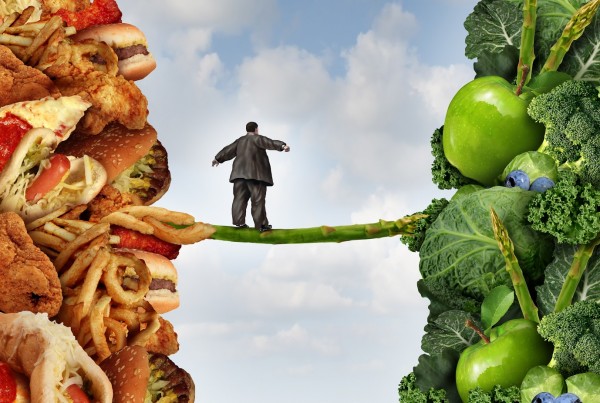 Diet change healthy lifestyle concept and having the courage to accept the challenge of losing weight and fighting obesity and diabetes as an overweight person walking on a highwire asparagus from fatty food towards vegetables and fruit.