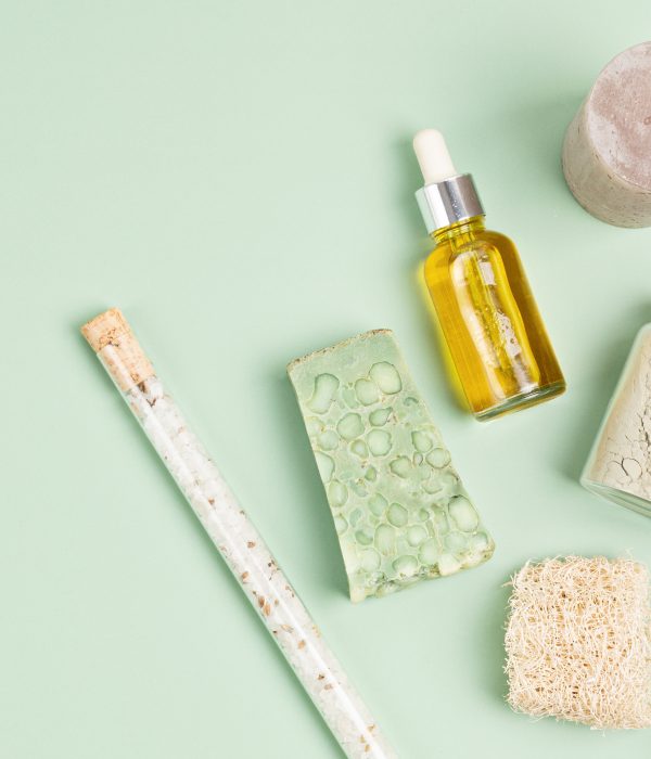 Cosmetics branding mockup. Bottles of eucalyptus essential oil, soap bar, fresh eucalyptus branches on green background. Natual organic ingredients for cosmetics, skin care, body treatment. Flat lay